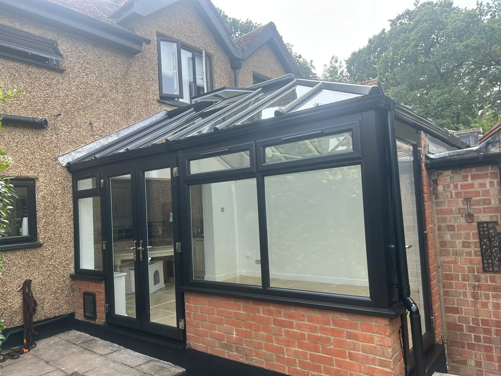 Completed conservatory from the garden — black uPVC frames on a red brick base, pitched glass roof, against a pebbledashed house