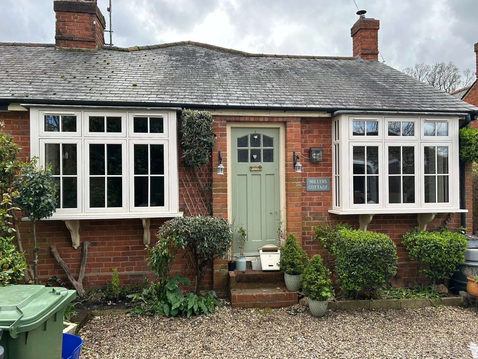 White uPVC casement windows with Georgian bars on a brick cottage, either side of a sage green front door