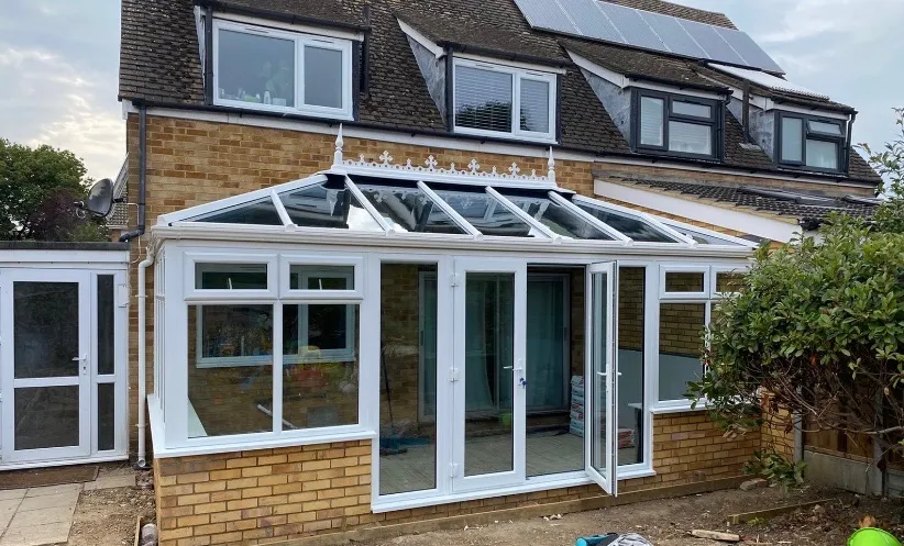 White uPVC Edwardian conservatory with a glass roof and open French doors, on low brick walls at the back of a house